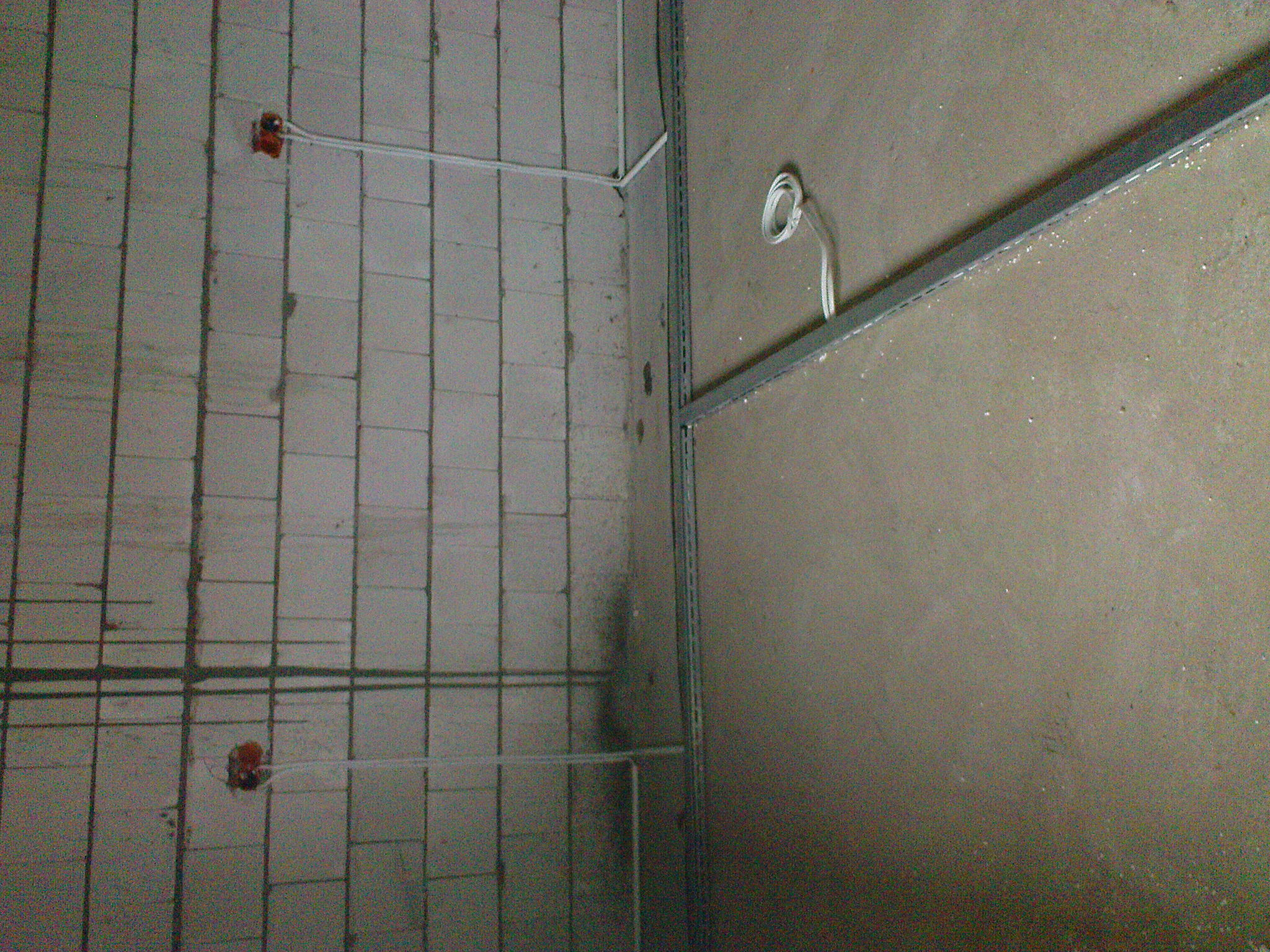 Surowa ściana z bloczków z widocznymi puszkami instalacyjnymi i przewodami elektrycznymi, obok ściana z metalowym profilem.